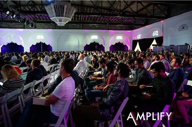 A large group of attendee's at Amplify Conference attendee's sat intently listening and watching a presentation