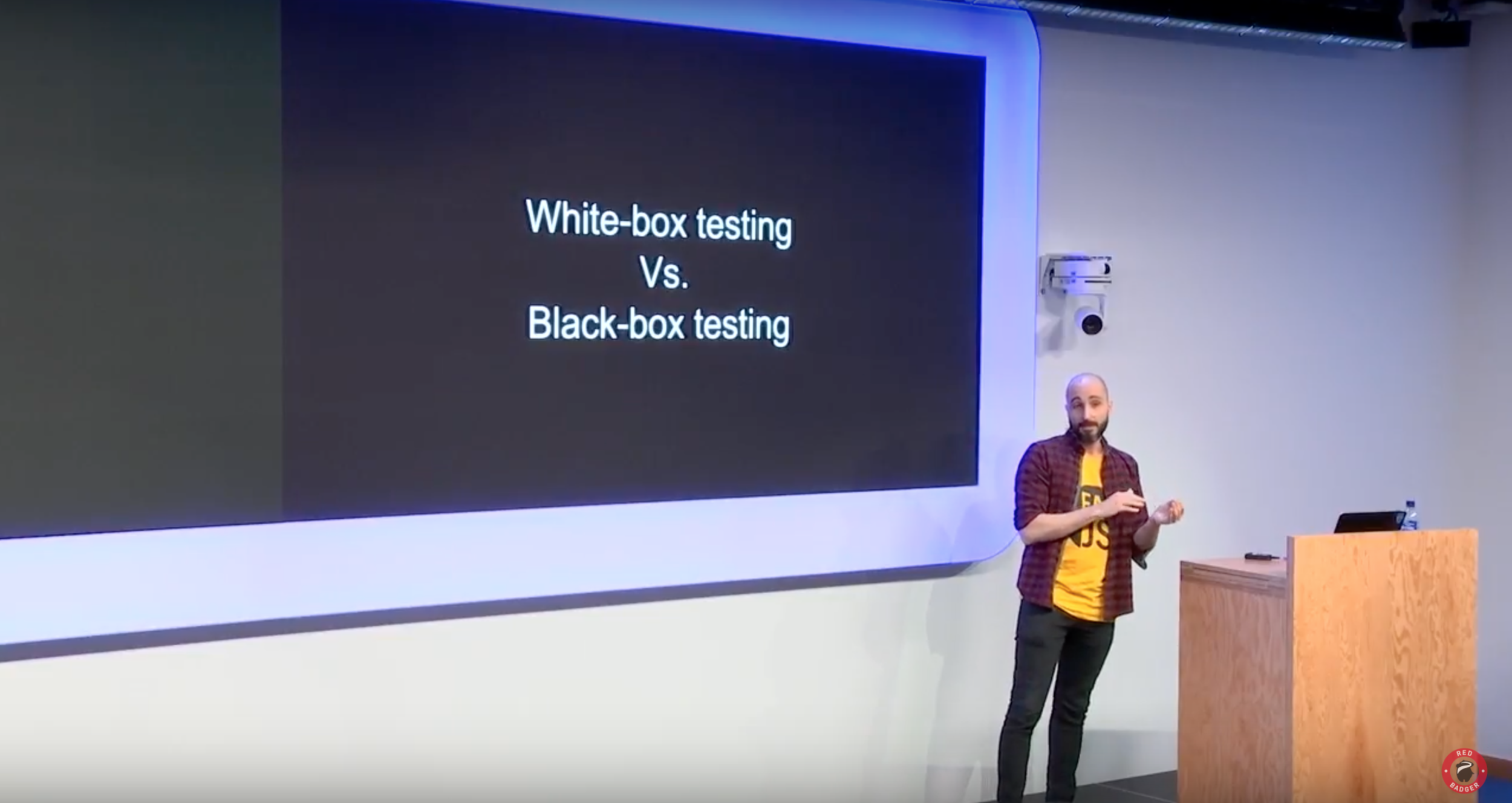 A photo from the presentation where the speaker is stood beside the slide which says "White-box testing vs Black-box testing"