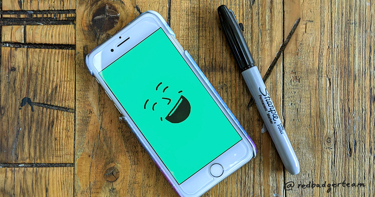 Illustration of laughing face on green background on a phone which is sat on a wooden table with a sharpie pen next to it