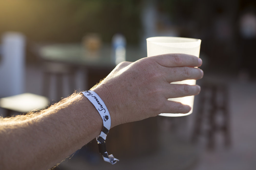 A closeup shot of a hand holding a drink with the 'Summer Party' wristband